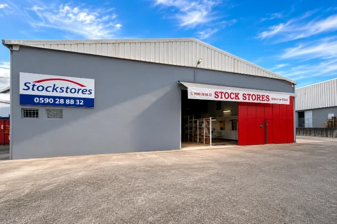 Atelier Stock Stores à Jarry, façade grise avec enseigne et grande porte rouge