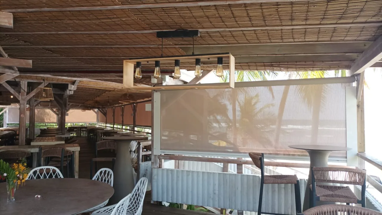 Store vertical à coulisses en toile screen protégeant la terrasse d'un restaurant en bord de mer